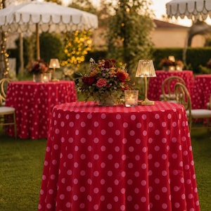 May include: Outdoor event setting with round tables covered in red polka dot tablecloths. Each table is decorated with floral arrangements, lamps, and candles. White scalloped umbrellas provide shade, creating an elegant ambiance for a garden party.