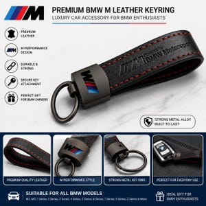May include: A black leather keyring featuring red stitching and the BMW M logo. The metal hardware is dark grey, and the leather strap is embossed with the text Powered By BMW Motorsport. The design includes a circular metal ring for key attachment.