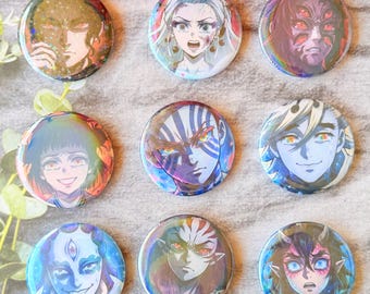 May include: A set of nine circular pin-back buttons featuring colorful anime-style character illustrations. Each button displays a unique portrait with distinct facial expressions, vibrant hair colors, and detailed features, arranged in a three-by-three grid.