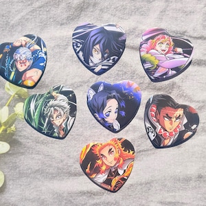 May include: Seven heart-shaped pop sockets featuring anime characters. Each pop socket has a different character design with vibrant colors. The characters are set against various backgrounds, including dark blue, green, and black.