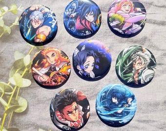 May include: A collection of seven round anime character buttons. Each button features a different character with vibrant colors and detailed artwork. The buttons are arranged on a light gray surface, showcasing the variety of designs.