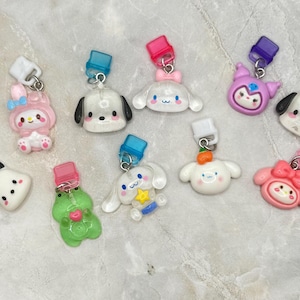 May include: A collection of colorful, cartoon character-themed clips. The clips feature various designs, including a pink bunny, a white dog, a blue and white character with a star, and a green frog. Each clip has a silver metal clasp and a colored plastic top.