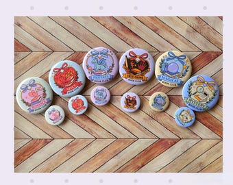 May include: A collection of colorful book club themed pinback buttons. The buttons feature illustrations and text such as "Romance", "Spicy", "Fantasy", "True Crime", "Magical", and "Mystery". The buttons are arranged on a wooden surface.