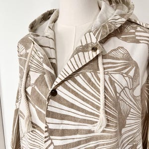 May include: A hooded jacket with a botanical leaf pattern in shades of brown and white. The jacket features a drawstring hood, a button-up front, and a neutral-colored lining. The jacket is displayed on a mannequin.