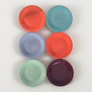 Puede incluir: Un conjunto de seis platos redondos de cerámica dispuestos en dos columnas. Los platos presentan un diseño de anillos concéntricos en el borde y vienen en varios colores, incluyendo coral, turquesa, azul claro, naranja, verde claro y morado.