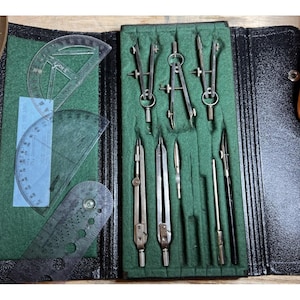 May include: A vintage drafting set in a black leather case. The set includes compasses, dividers, and protractors. The tools are made of metal and are arranged on a green felt background. The case is open, revealing the tools.