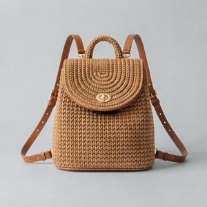 Puede incluir: Una mochila de ganchillo color canela con silueta estructurada, asa superior y cierre de solapa asegurado con un cierre giratorio de metal dorado. La bolsa incluye correas ajustables de cuero marrón con hebillas doradas.