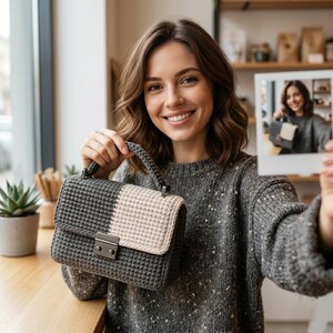 May include: A gray and cream-colored crochet handbag with a silver clasp and handle. The bag is held up by a person. A small succulent plant is in the background. A photo of the person holding the bag is also in the image.
