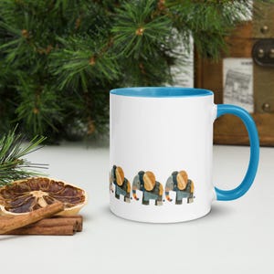 May include: White ceramic mug with a blue interior and handle. The mug features a repeating pattern of watercolour elephants in shades of blue, orange, and grey. The mug is set against a background of greenery and a wooden chest.