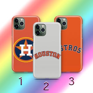 Puede incluir: Tres fundas para teléfono con diseños de los Astros de Houston. Las fundas son naranjas y blancas, con el logotipo del equipo y la palabra "HOUSTON" en una fuente curva. Las fundas están numeradas 1, 2 y 3.