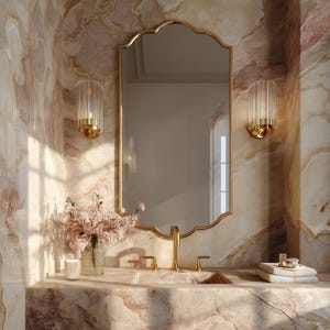 Puede incluir: Un lujoso baño con espejo dorado, apliques a juego y tocador de mármol. Un jarrón con flores rosas y una vela encendida añaden un toque de elegancia. Las paredes están adornadas con baldosas con vetas de mármol, creando un espacio elegante.