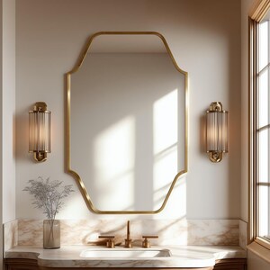 May include: A wall-mounted mirror with a gold-toned frame featuring a unique octagonal shape with rounded corners. The mirror is flanked by two cylindrical wall sconces with ribbed glass shades and gold-toned metal hardware.