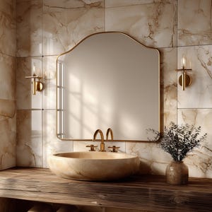 Peut inclure: Un meuble de salle de bain avec un miroir arrondi à cadre doré, une vasque en pierre beige avec un robinet doré et deux appliques murales dorées. L'ensemble est posé sur un comptoir en bois sombre avec des serviettes devant un carrelage marbré.