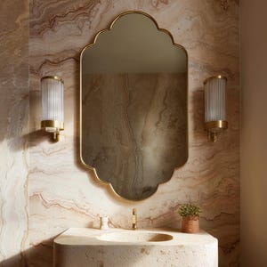 Peut inclure: Intérieur de salle de bain avec miroir doré à bordure festonnée, lavabo en pierre et deux appliques murales. Les appliques ont des abat-jours en verre cannelé et des bases dorées. Le mur présente un motif marbré.