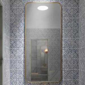 May include: A bathroom interior featuring a rectangular mirror with a gold frame above a marble sink. The walls are adorned with blue and white patterned tiles. A gold faucet and a circular ceiling light complete the scene.
