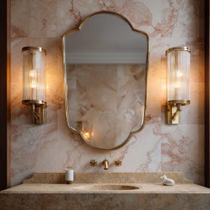 Peut inclure: Intérieur de salle de bain luxueux avec un miroir doré et des appliques murales assorties avec des abat-jours en verre cannelé. Le lavabo est en marbre, avec des robinets dorés et une petite figurine décorative de chat.