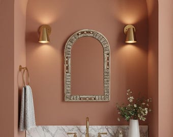 May include: A bathroom vanity with a marble countertop, a white sink, and a gold faucet. Above the sink is a decorative mirror with a white and beige frame. Two gold sconces flank the mirror, and a towel hangs on a gold towel ring.