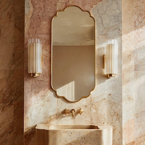 Peut inclure: Une salle de bain avec un miroir doré à bord festonné et des appliques murales cylindriques. Le lavabo et le robinet sont dorés, le tout sur un mur à effet marbré.