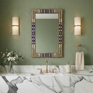 May include: A bathroom interior featuring a marble countertop with a gold faucet and fixtures. A rectangular mirror with a decorative frame hangs above the sink. Two wall sconces flank the mirror. A vase of flowers and a towel on a gold ring complete the scene.