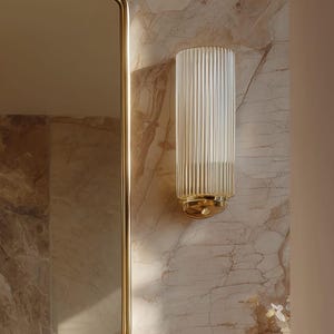 Peut inclure: Applique murale en verre transparent et cannel&eacute;, avec une base et des accents dor&eacute;s. L'applique est fix&eacute;e sur un mur &agrave; motifs de marbre, &agrave; c&ocirc;t&eacute; d'un miroir dor&eacute;. Le luminaire est de forme cylindrique.