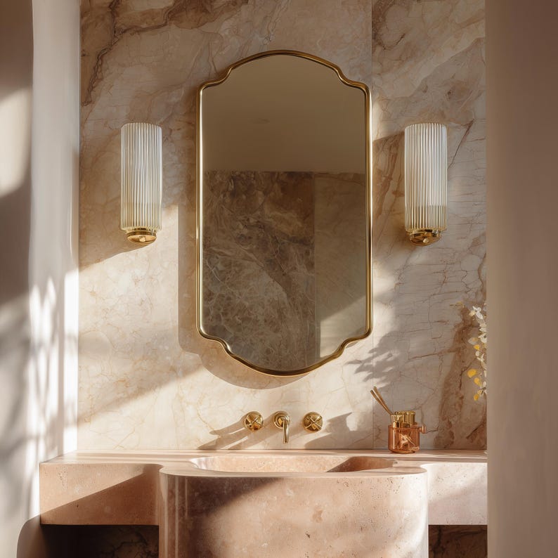 Peut inclure: Un meuble de salle de bain avec un miroir dor&eacute;, deux appliques murales et un lavabo en marbre rose. Le miroir a une forme unique et les appliques ont un design en verre cannel&eacute;. Le robinet et les autres accessoires sont dor&eacute;s.