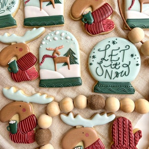 May include: A set of Christmas cookies decorated with moose, snow globes, and a "Let it Snow" message. The cookies are decorated with red, green, and white icing.