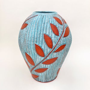 May include: A turquoise ceramic vase with a textured surface and a raised design of red leaves.