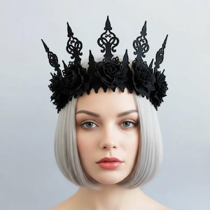May include: A black crown with intricate filigree and floral accents. The crown features a series of pointed spikes and is adorned with fabric roses. The headpiece is a gothic or fantasy-themed accessory.