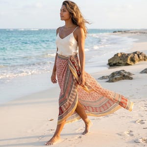 Puede incluir: Una camisola de color crema con tirantes finos combinada con una falda pareo larga y fluida con un estampado geométrico y de cachemira multicolor en tonos rosa, naranja y marrón, atada a la cintura con una abertura lateral.