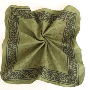 May include: A square olive green bandana featuring a dark brown border with a repeating paisley pattern and a central field decorated with a subtle, thin-lined brown floral motif. The fabric is folded in the centre, creating a soft, gathered texture.
