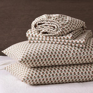 May include: A bedding set featuring two rectangular pillows and folded sheets stacked on top. The fabric is off-white with a repeating pattern of small, dark red flowers with green stems and leaves arranged in neat, vertical rows across the surface.