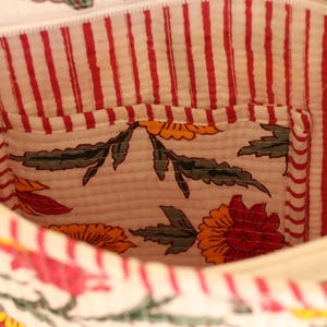May include: Interior view of a white fabric bag with a red and white striped lining. The bag features a small pocket with a floral pattern in red, yellow, and green. The bag's interior is visible.