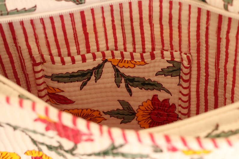 May include: Interior view of a white fabric bag with a red and white striped lining. The bag features a small pocket with a floral pattern in red, yellow, and green. The bag's interior is visible.