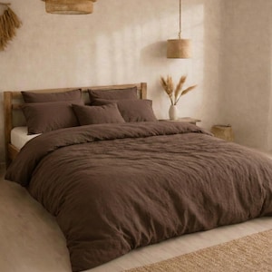 May include: A bed dressed with a brown duvet cover and matching pillowcases. The bed frame is light-coloured wood. The room has a neutral colour palette with a woven pendant light and a small rug.