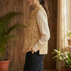 Puede incluir: Una mujer con un chaleco con estampado floral en beige, rojo, naranja y verde, sobre una camisa blanca de manga larga y pantalones azul oscuro. El conjunto se completa con botas marrones. El chaleco est&aacute; abrochado.