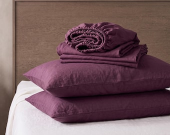 Puede incluir: Un juego de ropa de cama en color ciruela intenso que incluye dos almohadas rectangulares apiladas horizontalmente y una sábana bajera plegada encima. La tela tiene un tejido visible y ligeramente texturizado.