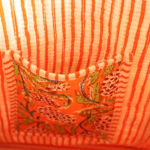 May include: Close-up of a fabric bag interior. The lining features vertical orange and white stripes. A pocket with a floral pattern in orange, green, and white is sewn into the lining. The bag's interior is brightly colored.