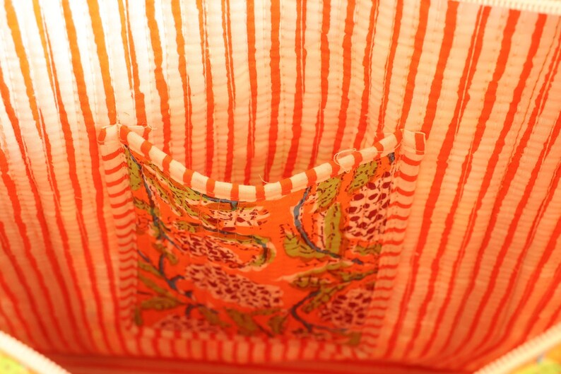 May include: Close-up of a fabric bag interior. The lining features vertical orange and white stripes. A pocket with a floral pattern in orange, green, and white is sewn into the lining. The bag's interior is brightly colored.