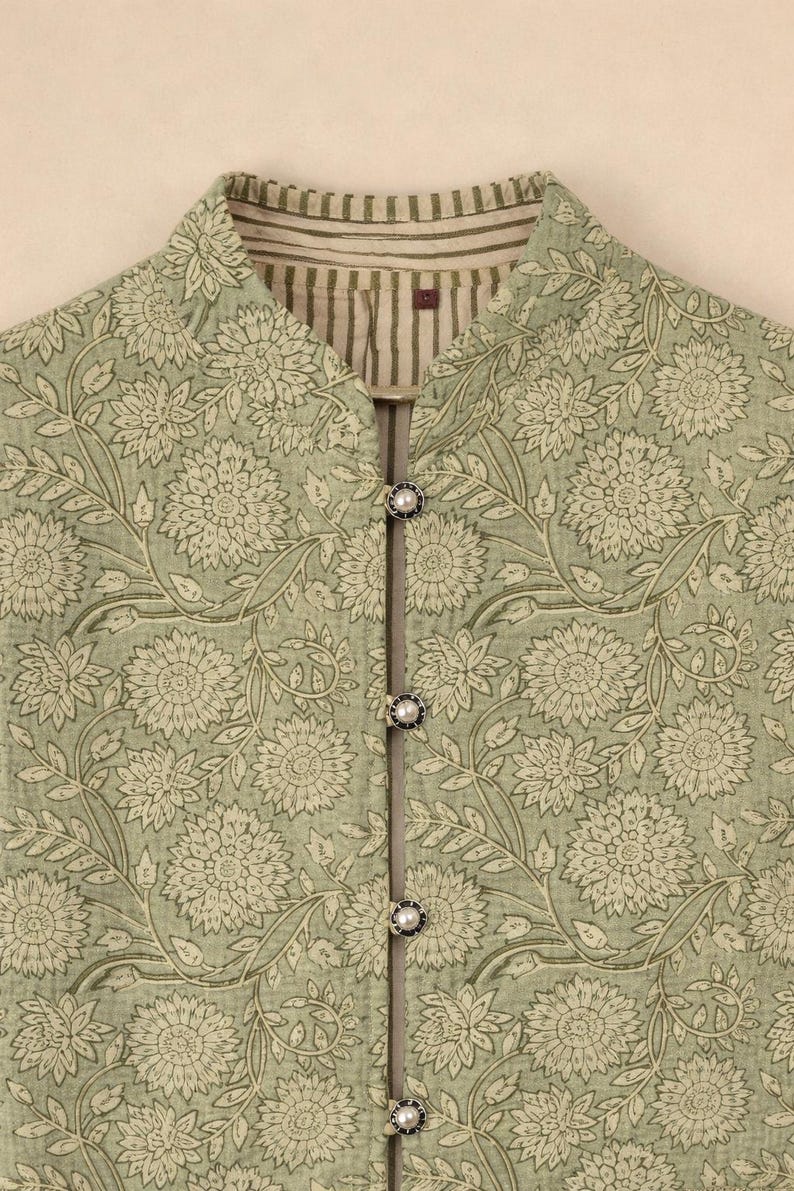May include: A light green floral print jacket with a mandarin collar and three pearl-like buttons. The jacket features a repeating pattern of large flowers and leaves in a muted color palette. The collar has a striped lining.