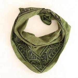 May include: A triangular olive green bandana featuring a dark brown border with a repeating paisley pattern and a central section decorated with small, delicate line-drawn botanical motifs including leaves, stems, and sun-like circular shapes.