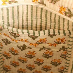 May include: Interior view of a tote bag with a floral pocket. The bag's lining features vertical green stripes on a cream background. The pocket is decorated with a repeating pattern of yellow flowers and green leaves.