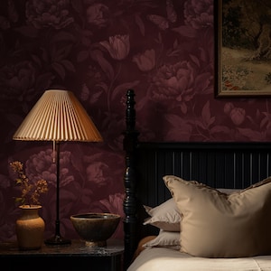 May include: A bedroom scene featuring a black bed frame, a nightstand with a lamp, and a floral wallpaper. The lamp has a pleated shade, and the wallpaper is a deep burgundy with floral patterns. The bed has beige pillows and a comforter.