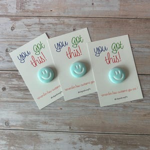 May include: Three light blue circular smiley face pins attached to white rectangular cards. Each card features the text "you got this!" in blue and red, with "remember how awesome you are!" and the social media handle @rubyandrosegifts printed below.