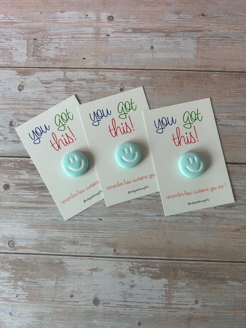 May include: Three light blue circular smiley face pins attached to white rectangular cards. Each card features the text "you got this!" in blue and red, with "remember how awesome you are!" and the social media handle @rubyandrosegifts printed below.