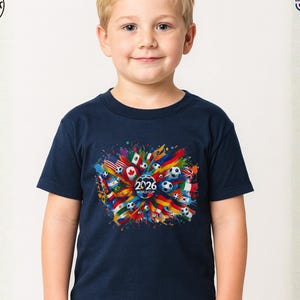 May include: Navy blue youth toddler t-shirt featuring a colorful graphic design for the 2026 World Cup. The design includes soccer balls, flags, and the text "2026 WORLD CUP". The shirt is made in the USA.