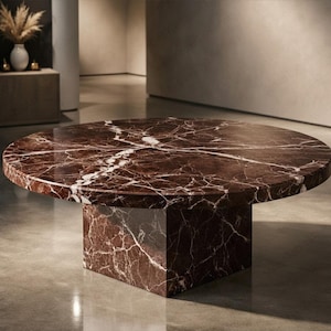 Può includere: Tavolino rotondo con piano in marmo marrone scuro e base quadrata. Il marmo presenta venature bianche. Il tavolo è un design moderno ed è ambientato in una stanza dai toni neutri. Il diametro del tavolo è di circa 120 cm.