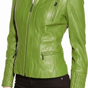 Puede incluir: Chaqueta de cuero verde lima con cremallera, cuello alzado y detalles acolchados en hombros y puños. La chaqueta tiene dos bolsillos con cremallera en el pecho y dos en la cintura. El modelo lleva pantalones negros.