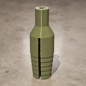 May include: An olive green 3D-printed object, featuring a cylindrical top and a tiered, conical base. A vertical slit runs down the side. It appears to be a component or part for a larger assembly.