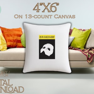 May include: A white square cushion with a cross-stitch design. The design features the word "BROADWAY" above a black rectangle with a white mask. The cushion is 10.16cm x 15.24cm on a 13-count canvas. Text reads "NEEDLEPOINT/ CROSS STITCH CHART DIGITAL DOWNLOAD".