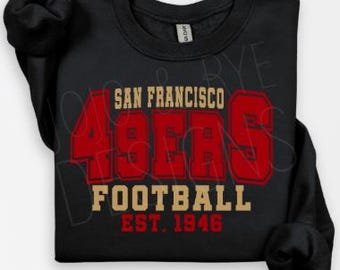 Può includere: Felpa nera con la scritta "SAN FRANCISCO 49ERS FOOTBALL EST. 1946" in rosso e oro. Il numero "49" è in grassetto, in rosso. La felpa ha un girocollo e maniche lunghe.